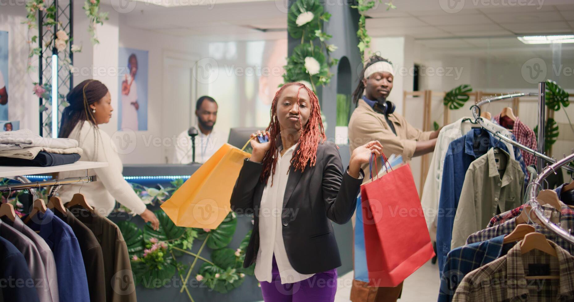 African american couple having fun in fashion boutique, doing dance moves. Jolly customers enjoying themselves to nice mall clothing store music, dancing with shopping bags photo
