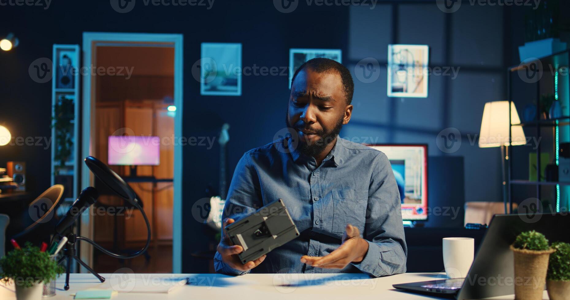 BIPOC content creator filming technology review of newly launched V mount battery, unpacking it and presenting specifications to audience. Internet star showing charging device to viewership photo