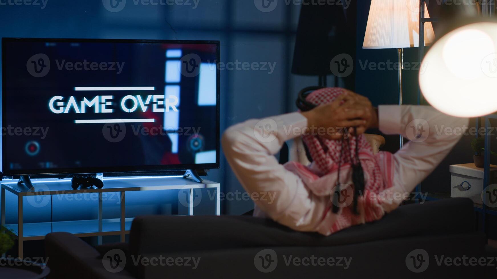 Man playing videogames on TV after long day at work angry after receiging game over screen. Muslim gamer upset after losing at science fiction shooter competition on gaming console photo