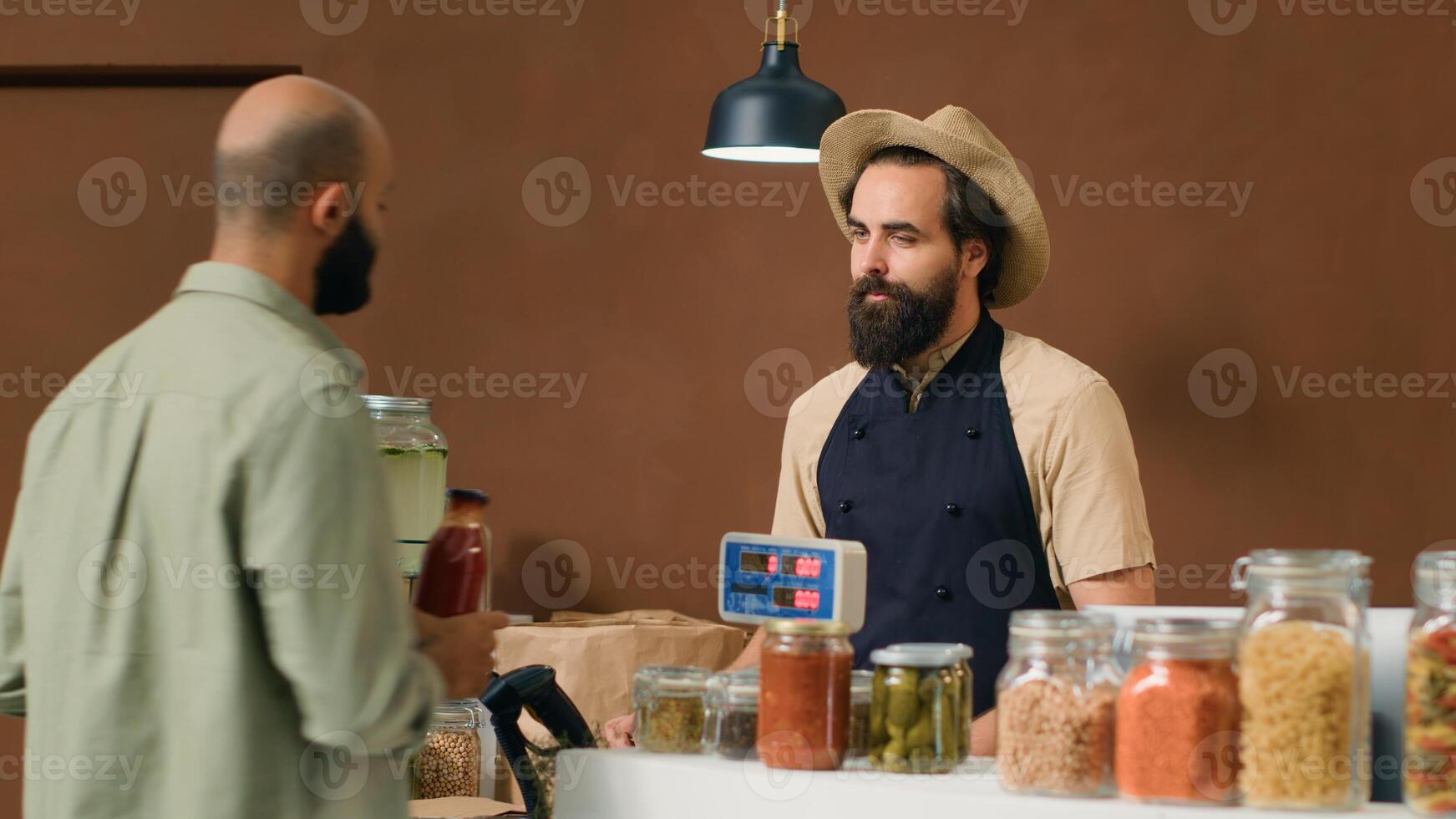 Vendor at checkout scanning and weighting products to sell to frequent client in local zero waste store. Young man placing vegetables on scale, selling locally grown produce to buyer. photo