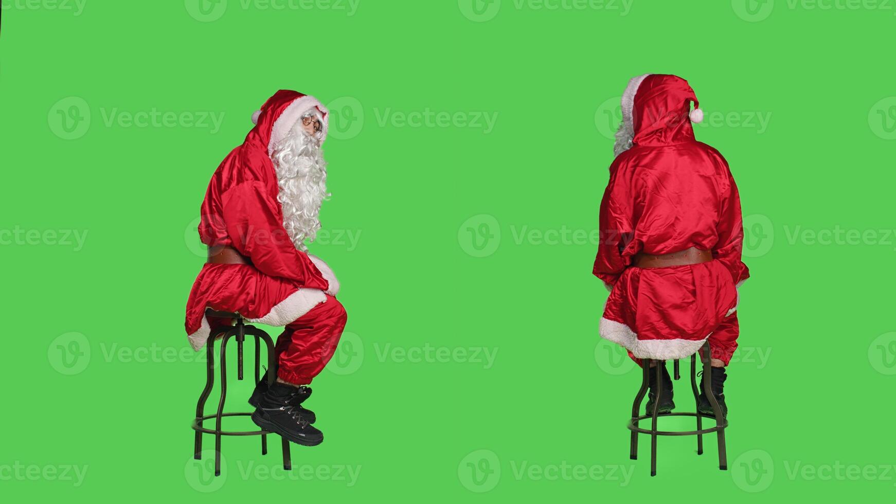 Santa claus on chair looking around, posing over greenscreen backdrop during christmas holiday. Model portraying saint nick character for december traditional celebration event. photo