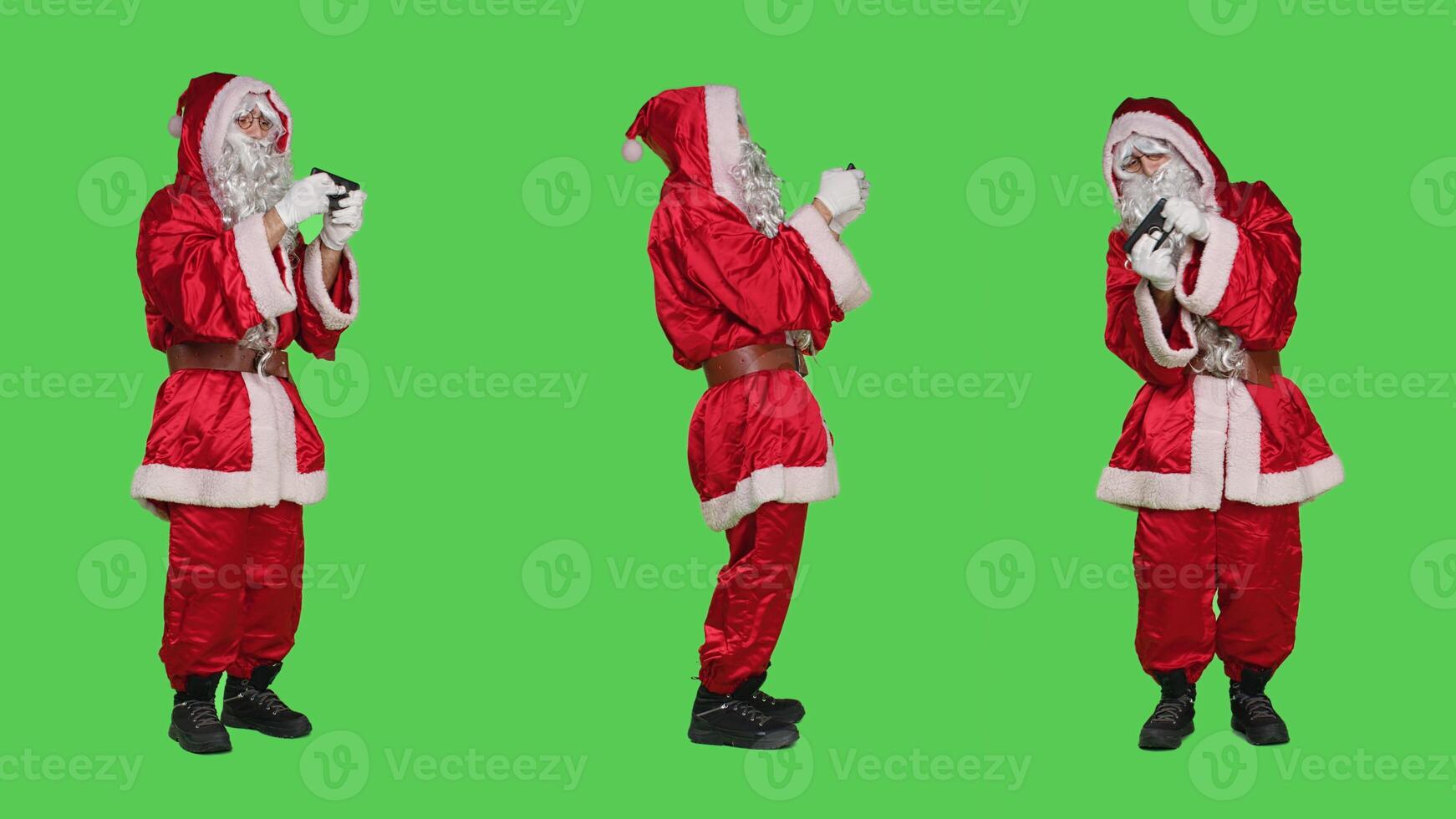 Santa claus having fun with videogames, playing online gaming competition and standing over full body greenscreen. Young cool saint nick character play mobile game on christmas eve. photo