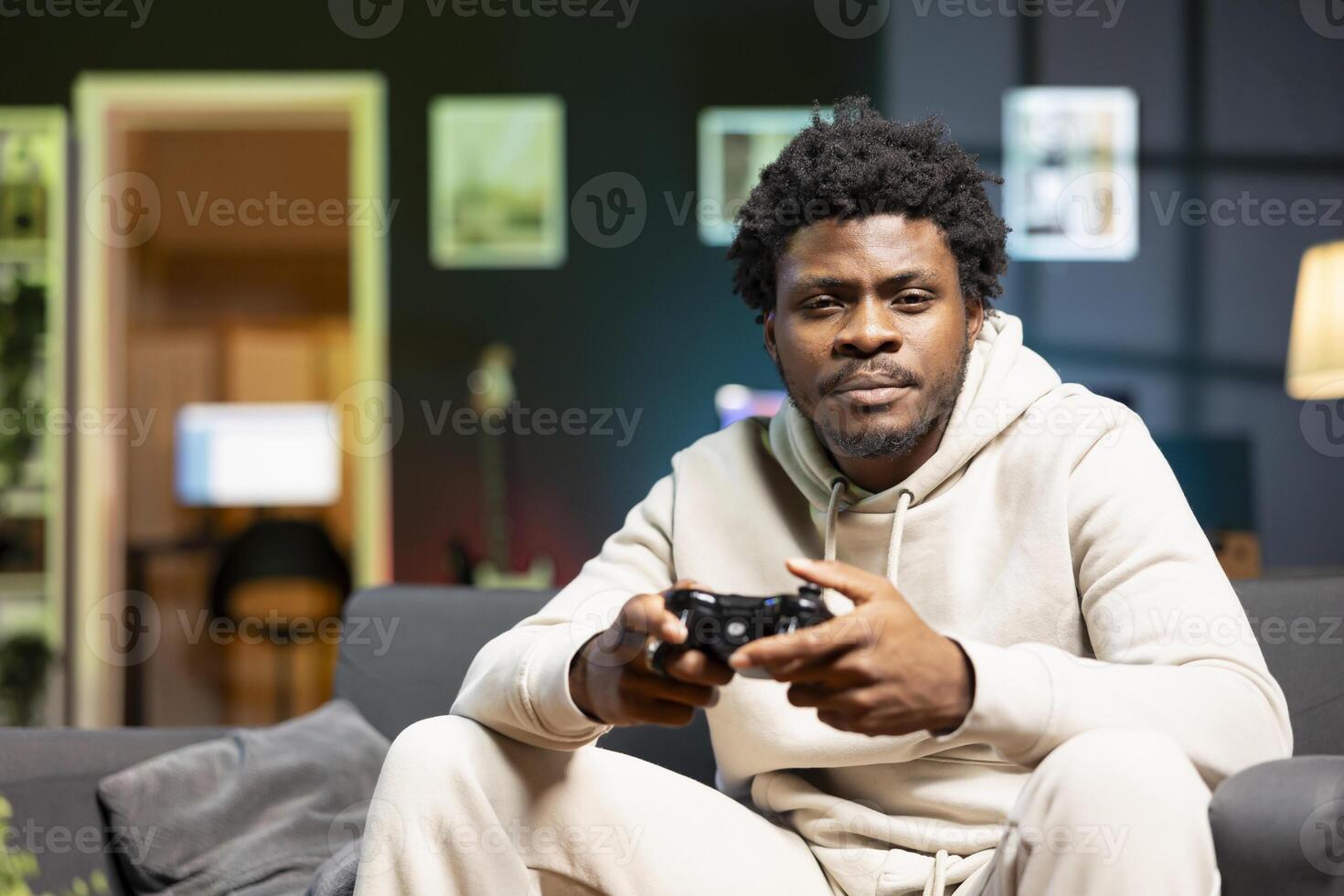 Man in rgb lit living room playing games on couch, enjoying day off from work. Gamer battling enemies in internet multiplayer shooter on gaming console, talking with teammates through headphones photo