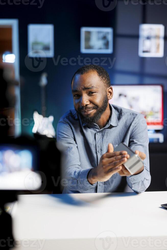Tech guru assessing portable speaker performance, expressing dissatisfaction with subpar components used. Man shoots Bluetooth audio device review for online channel, displeased with low quality photo
