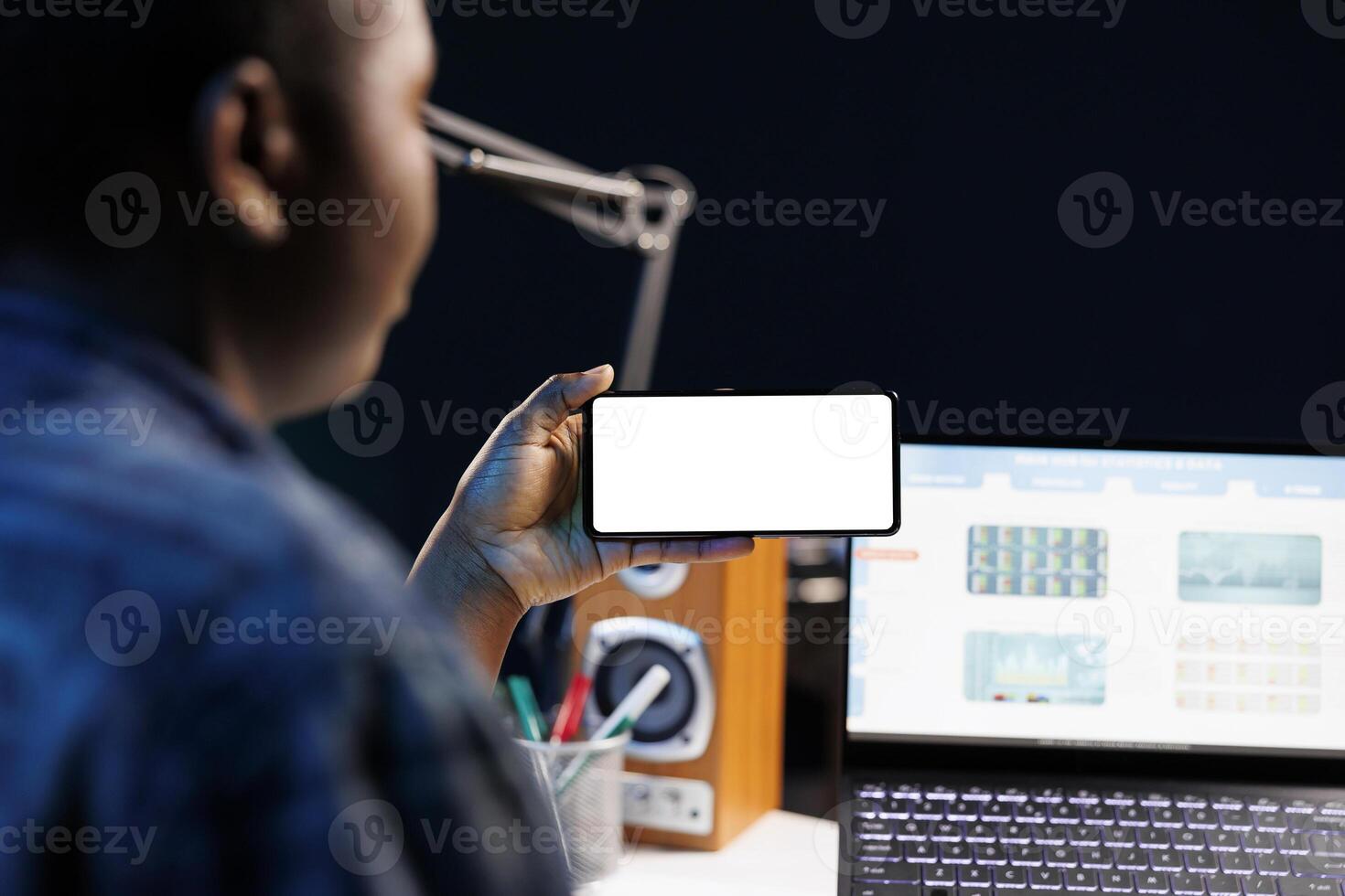 Close-up of freelancer working from home, using a laptop and smartphone displaying blank copyspace mockup template. Black woman looking at isolated white screen on mobile device. photo
