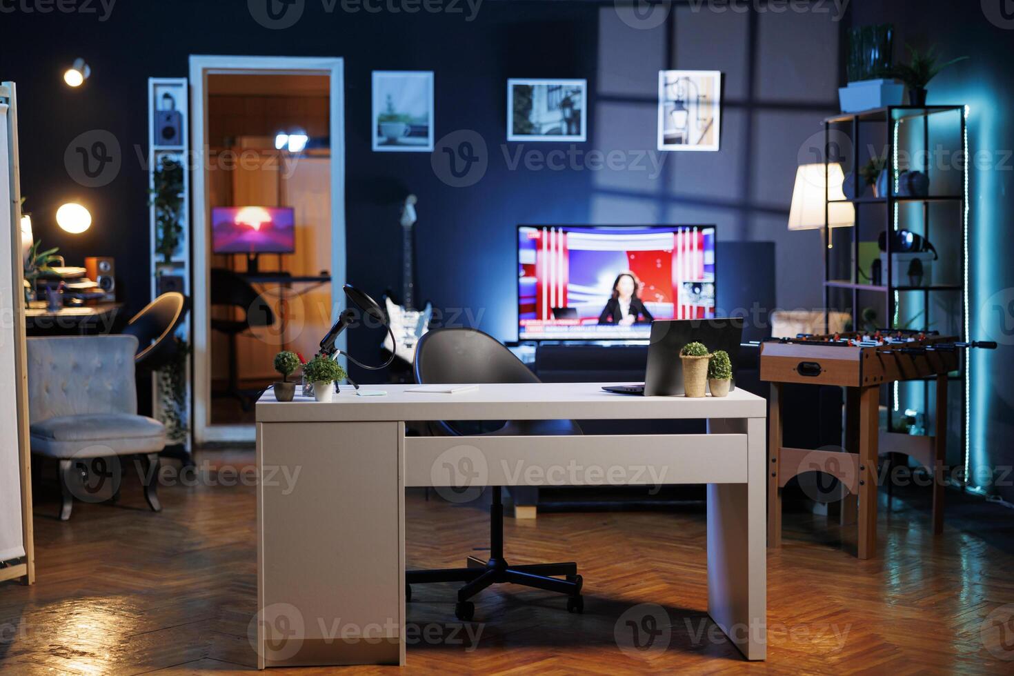 Empty stylish brightly lit home studio interior illuminated with neon lights at night and artwork decorating the walls. Clean apartment with TV running in background on news channel broadcast photo