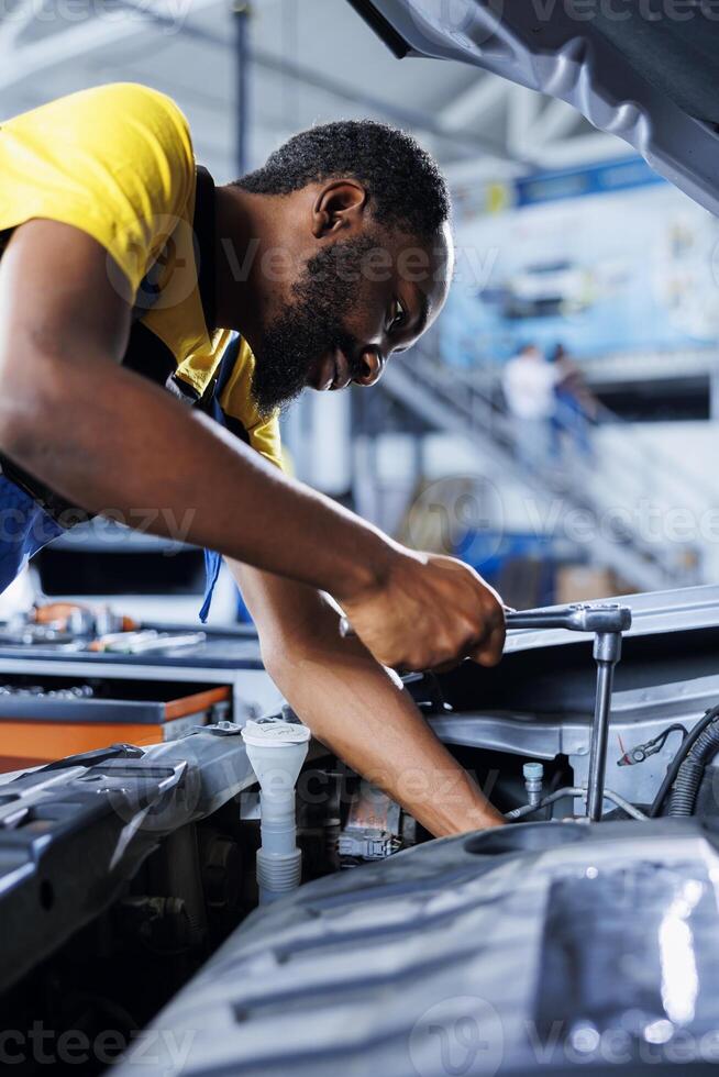 Repairman in car service using professional mechanical tool to repair broken engine. Capable worker in garage repairing client automobile, ensuring optimal automotive performance photo