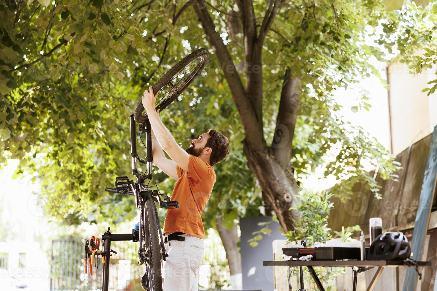 Energetic caucasian male dismantling damaged bicycle tire to repair and replace with new. Young athletic man grasping and carrying bike wheel for further maintenance in home yard. photo