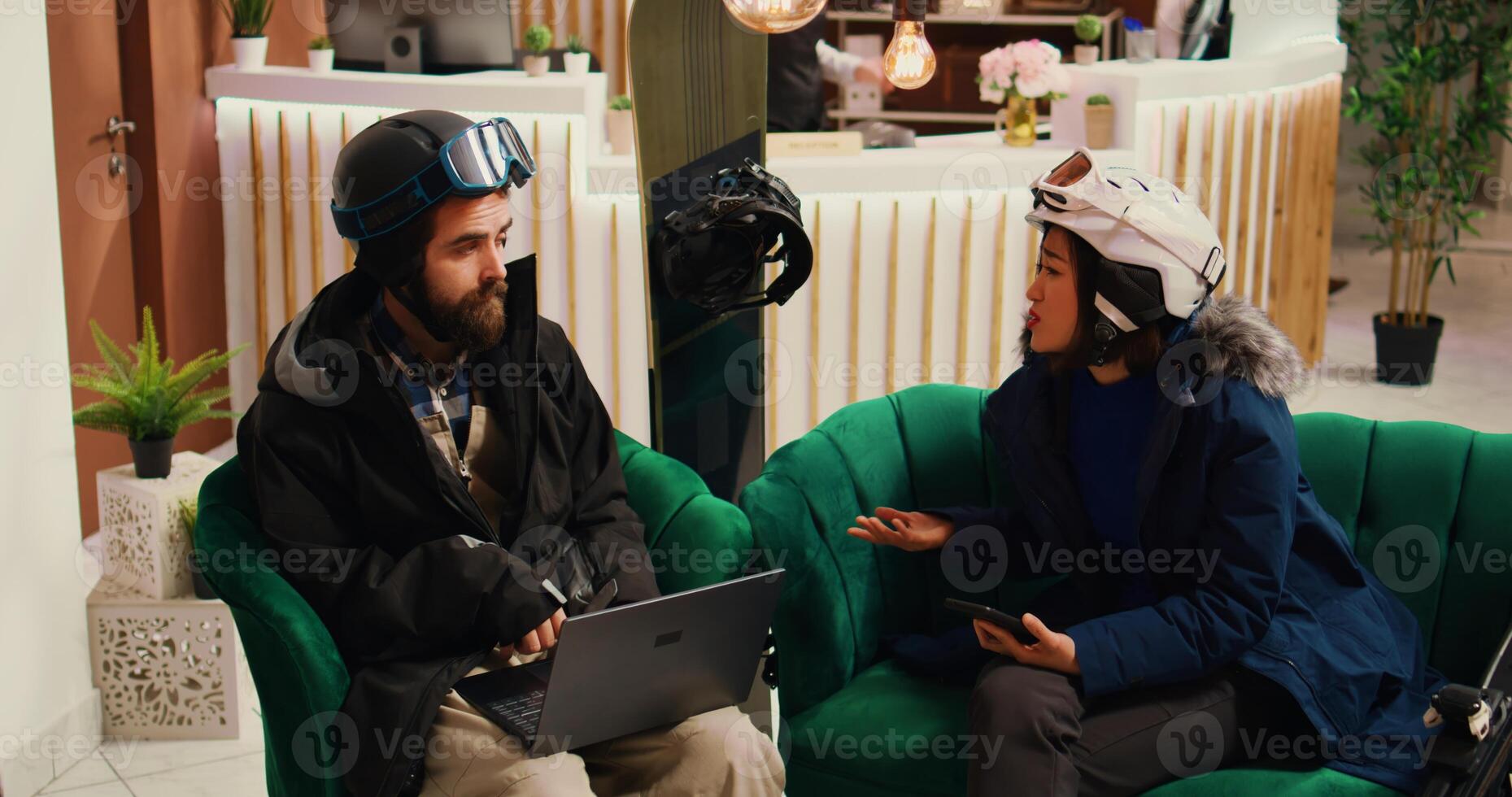 Modern people using devices at hotel, arriving at ski mountain resort during cold season. Boyfriend searches for slope reviews online while girlfriend checks text messages. Handheld shot. photo