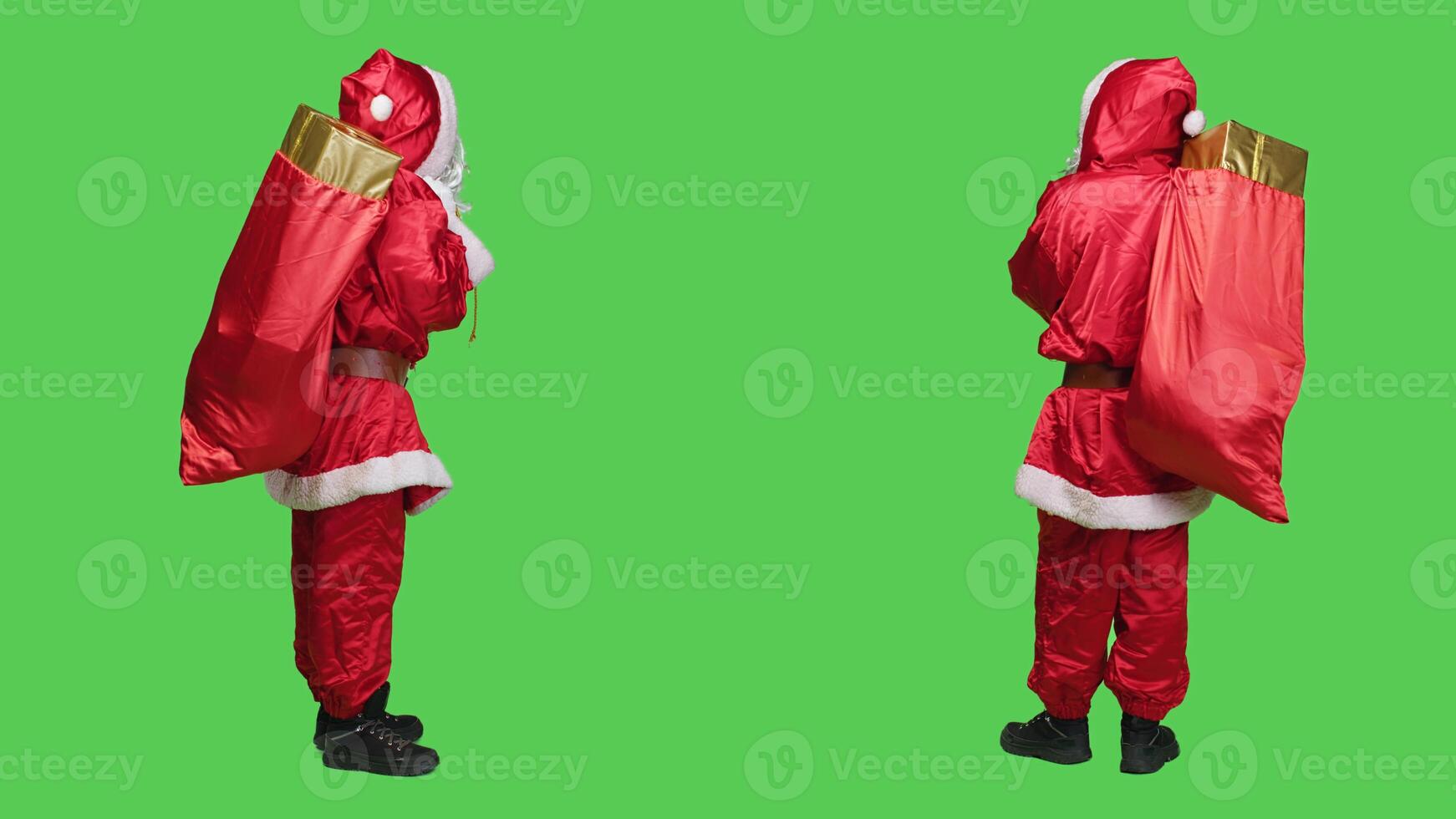 Santa carrying red sack of gift boxes in studio with full body greenscreen backdrop, preparing to deliver toys to children. Young adult portraying saint nick with bag of presents, xmas spirit. photo