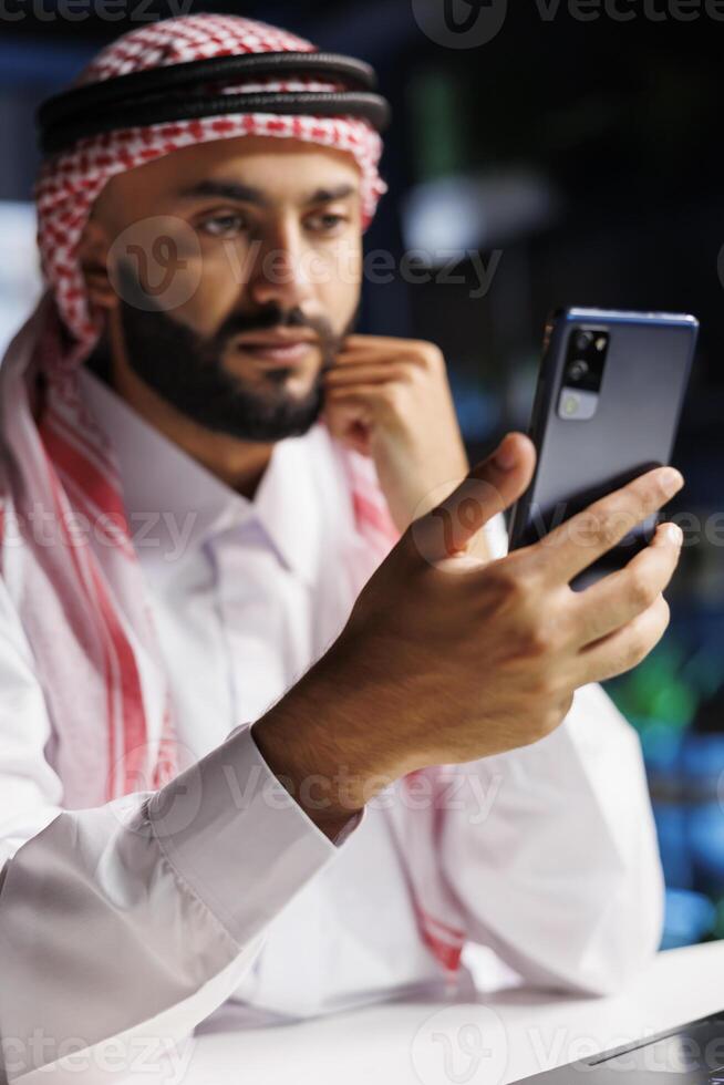 Close-up shot of Middle Eastern male adult holding his cell phone for a conference call. Detailed view of a youthful Muslim man surfing the net on his digital mobile device. photo
