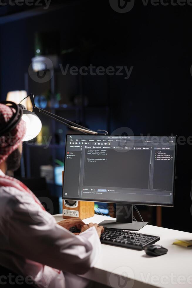 Traditional Middle Eastern developer compiles code on desktop computer, showcasing expertise in programming, algorithms, and software development. Selective focus on pc monitor displaying source code. photo