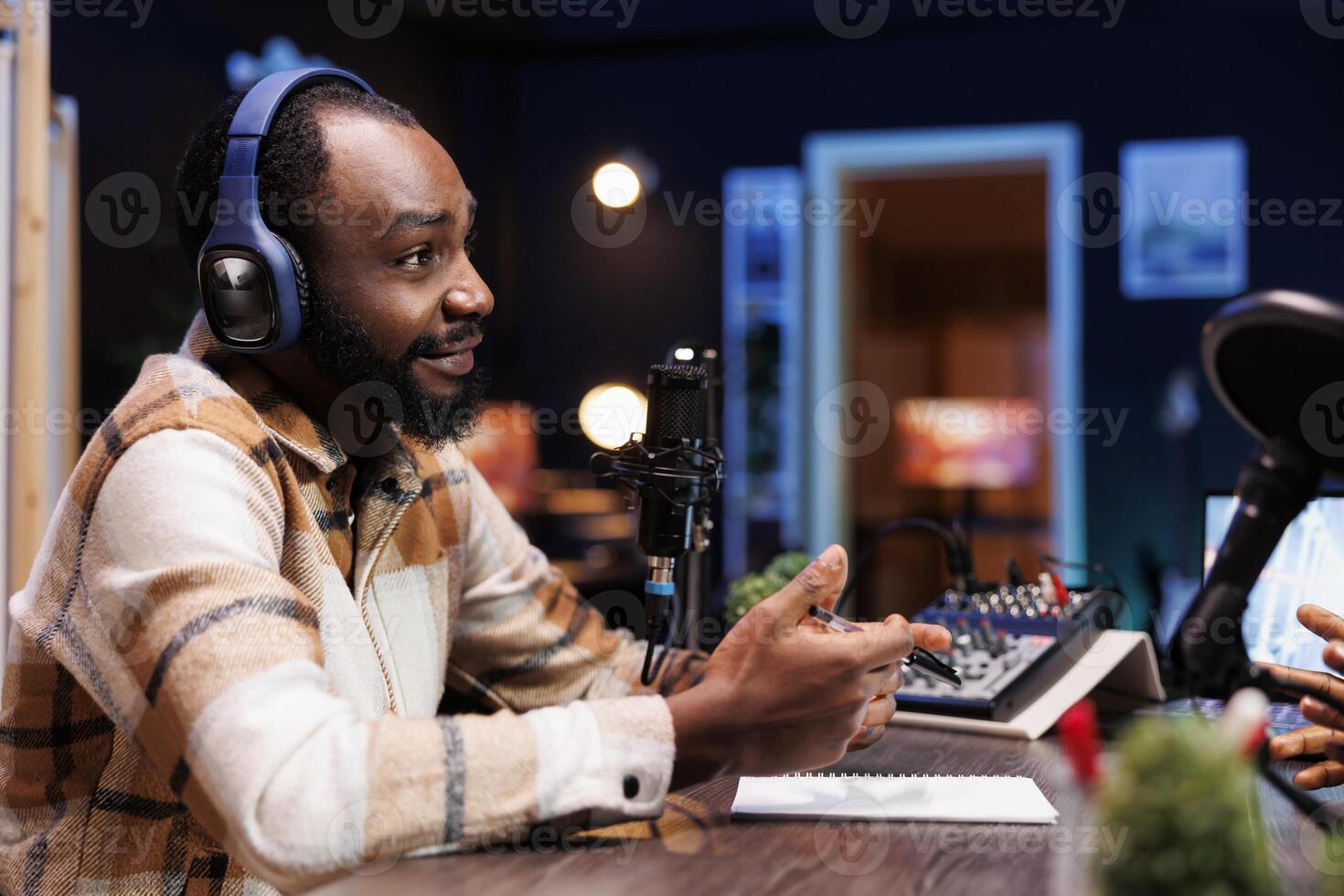 African American guy is speaking into microphone while conducting online radio show. A podcast episode featuring a black man host doing an interview in his home studio for internet audience. photo