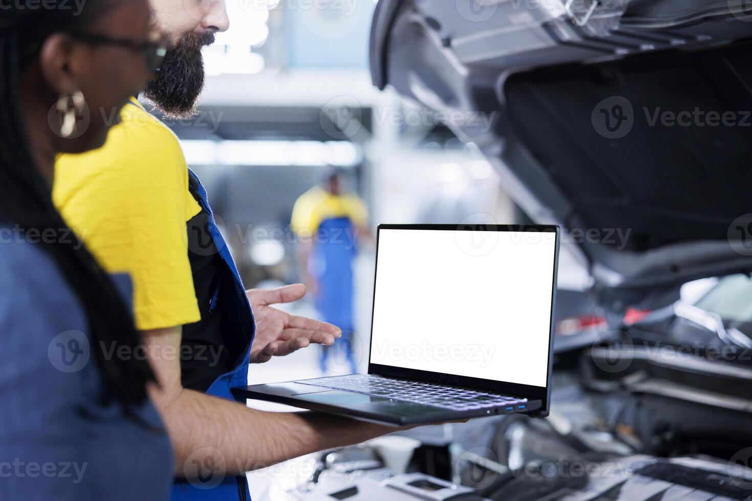 Repairman in garage using mockup laptop to follow checklist while doing maintenance on african american woman car. Expert in repair shop does checkup on client vehicle helped by isolated screen device photo