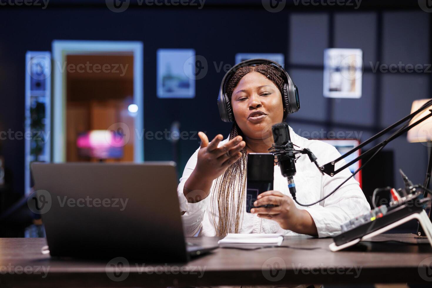 African american female influencer presenting newly released mobile device for her social media channels. Black woman sitting at table and speaking into a microphone while describing new smartphone. photo