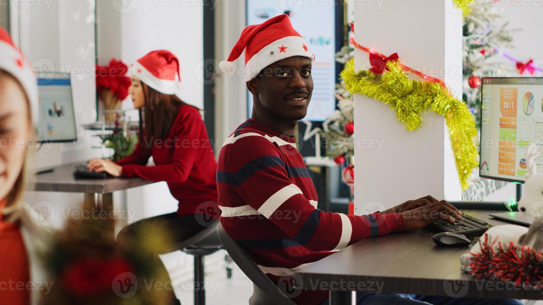 Portrait of friendly african american startup employee checking documents for accuracy in decorated office during Christmas. Workers solving tasks at workstation in multiracial workspace photo