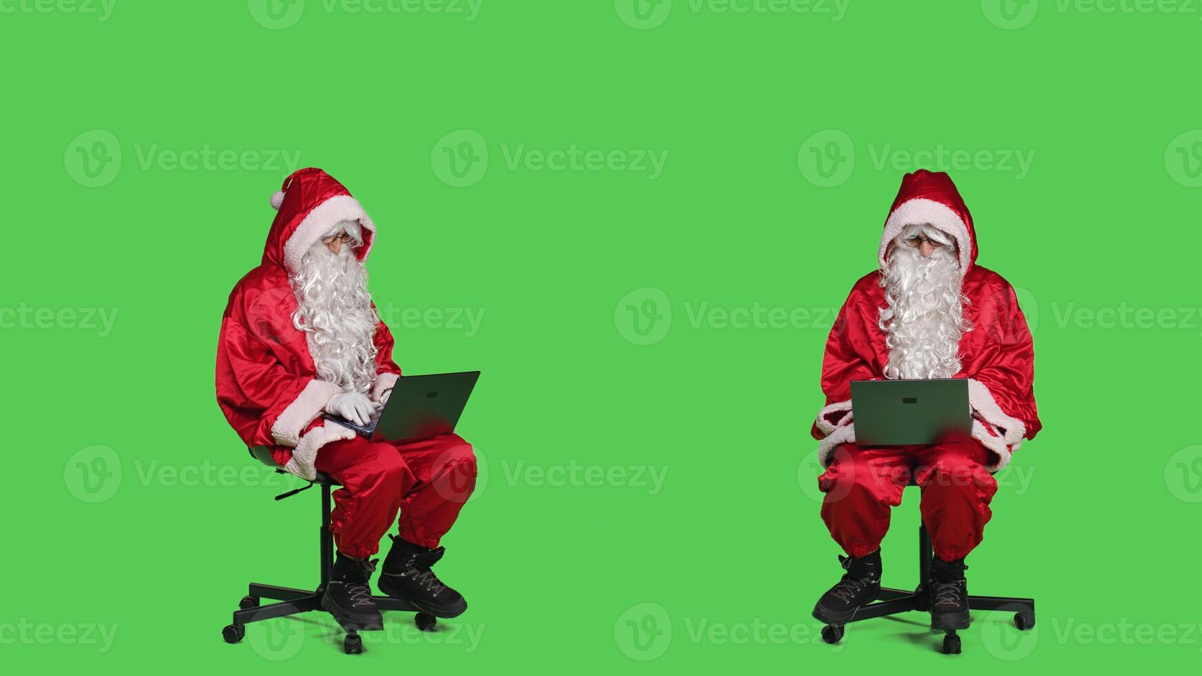 Cool saint nick using laptop on chair, sitting against full body greenscreen backdrop in studio. Father christmas working with modern portable pc, browsing online website in red costume. photo