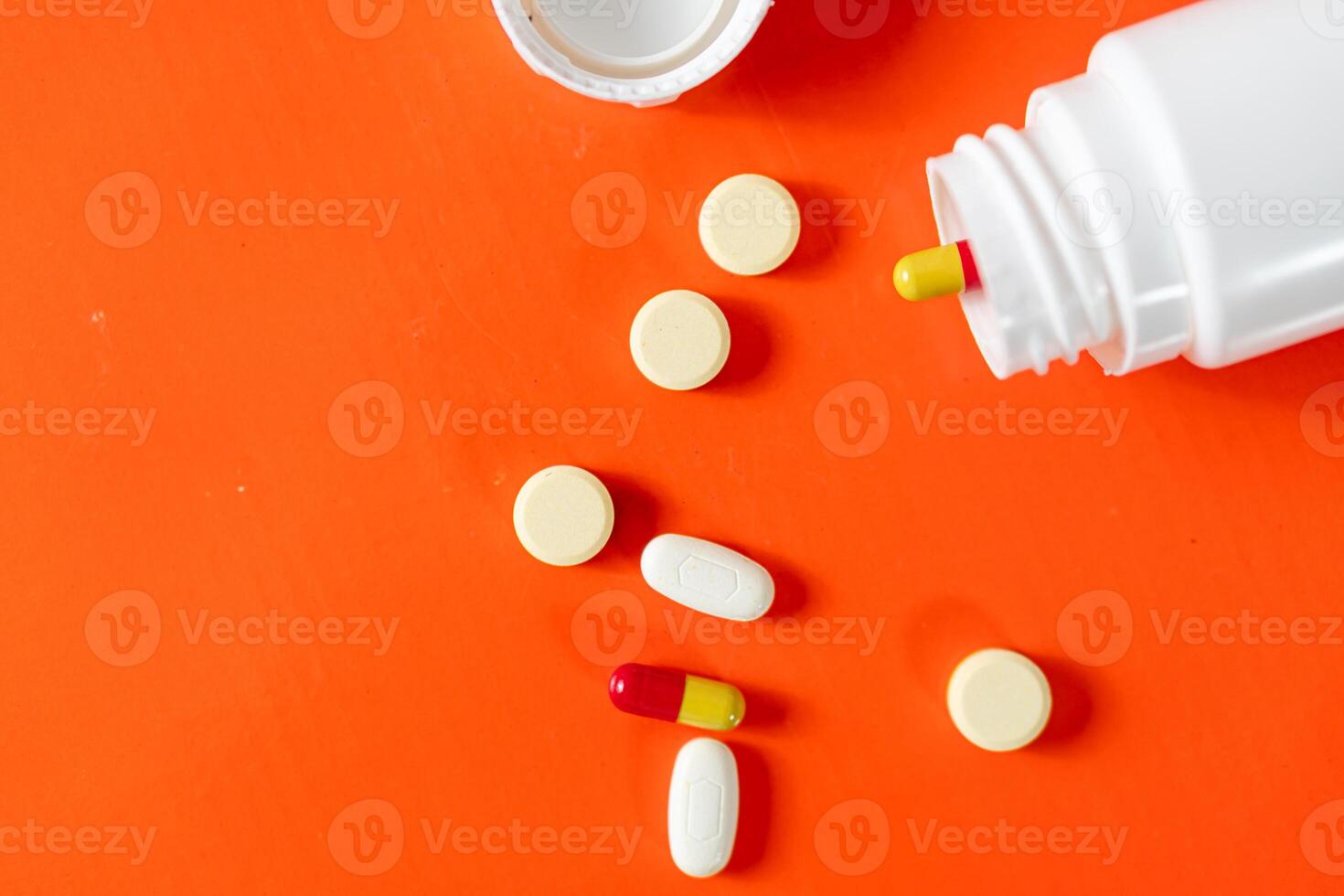 Pills and capsules spilled from a bottle on orange background photo