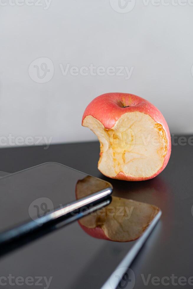Bitten Apple Next to Smart phone on Reflective Surface photo