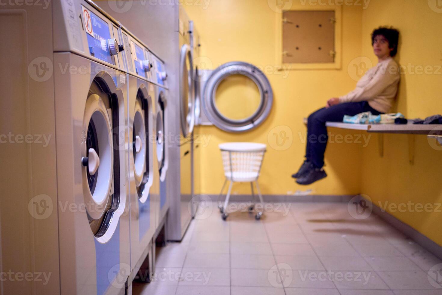 young plus size woman loads clothes into a washing machine in a laundry room in the basement of a student dormitory photo