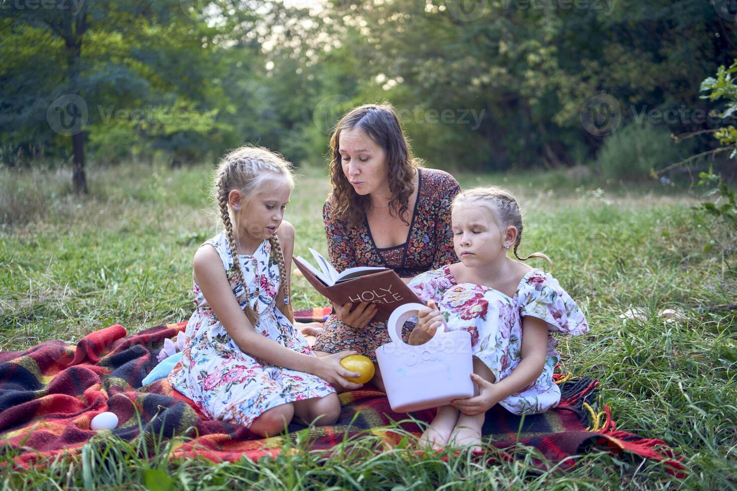 a mother and her two daughters read the holy bible and pray at an Easter picnic photo