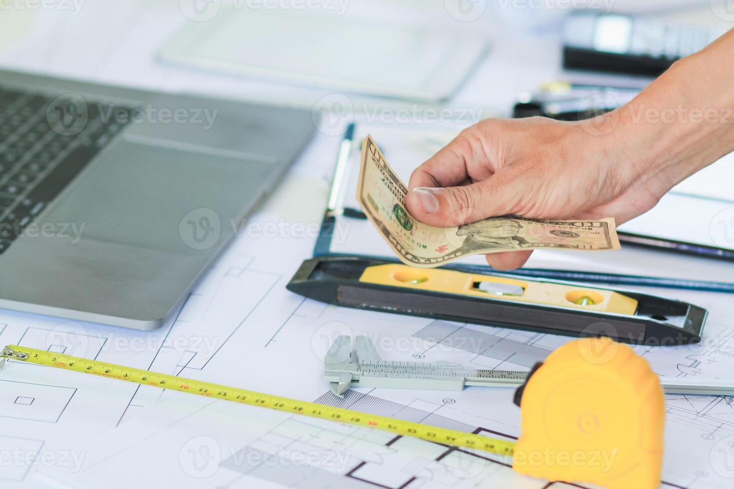 Engineers and Foreman are calculating workers' expenses and overtime to pay workers compensation and overtime each month. Foreman holds cash in hand to pay workers as compensation photo