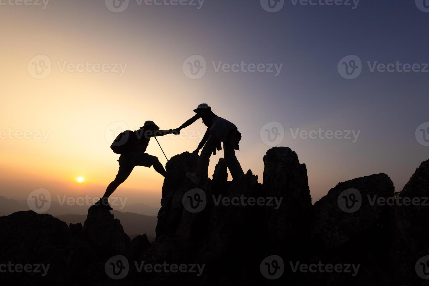 Two hikers helping each other climb a mountain at sunrise. Helping each other. Climbing. Rescue and teamwork concept. Helping hand in the mountains. photo