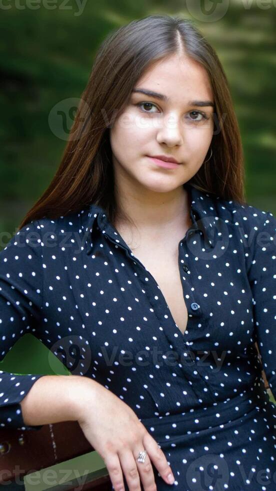 Emotional girl teenager with long hair hairstyle braids in a green shirt sits on a bench in the park. photo