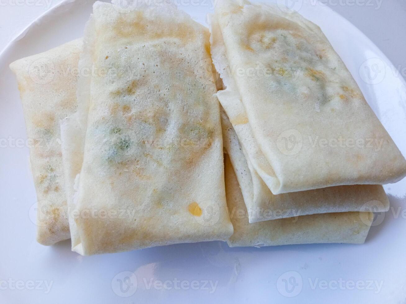 Martabak Telur Kulit Lumpia, crispy snacks filled with eggs, meat, and scallions wrapped in spring roll skin. Favorite street food eaten with green chili. before being fried on a white plate photo