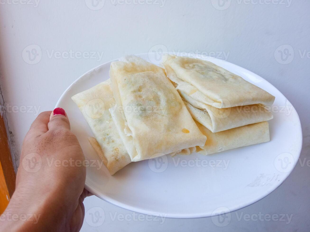 Martabak Telur Kulit Lumpia, crispy snacks filled with eggs, meat, and scallions wrapped in spring roll skin. Favorite street food eaten with green chili. before being fried on a white plate photo