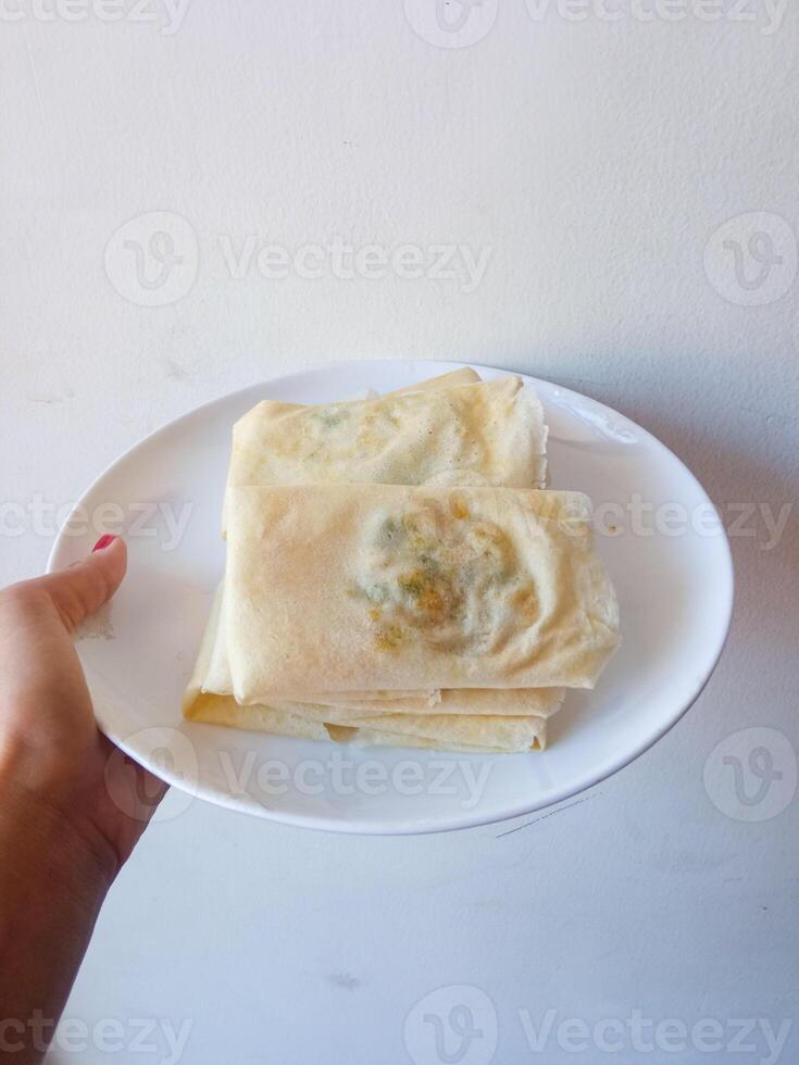 Martabak Telur Kulit Lumpia, crispy snacks filled with eggs, meat, and scallions wrapped in spring roll skin. Favorite street food eaten with green chili. before being fried on a white plate photo