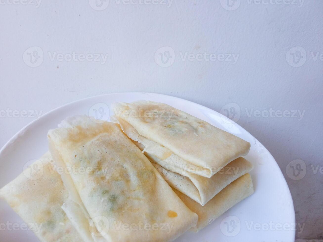 Martabak Telur Kulit Lumpia, crispy snacks filled with eggs, meat, and scallions wrapped in spring roll skin. Favorite street food eaten with green chili. before being fried on a white plate photo