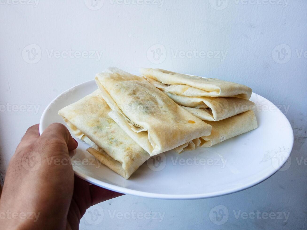 Martabak Telur Kulit Lumpia, crispy snacks filled with eggs, meat, and scallions wrapped in spring roll skin. Favorite street food eaten with green chili. before being fried on a white plate photo