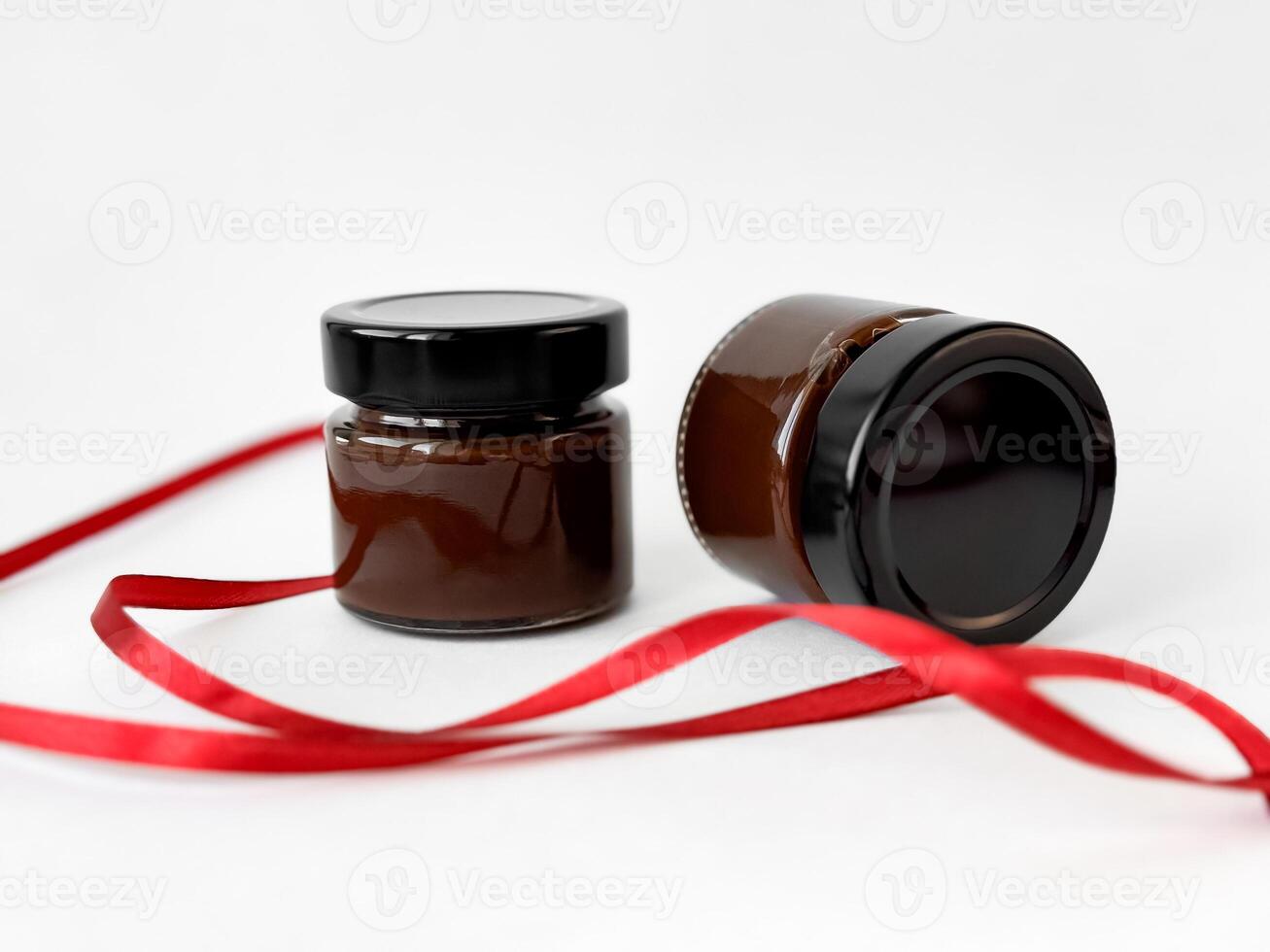 Elegant glass jars with chocolate spread with red ribbon on white background for gift packaging photo