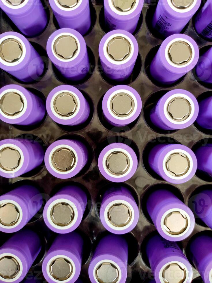 A closeup of neatly arranged cylindrical lithium-ion batteries in a vibrant purple with a metallic finish. Each battery displays clear positive terminals, creating a visually striking grid. photo