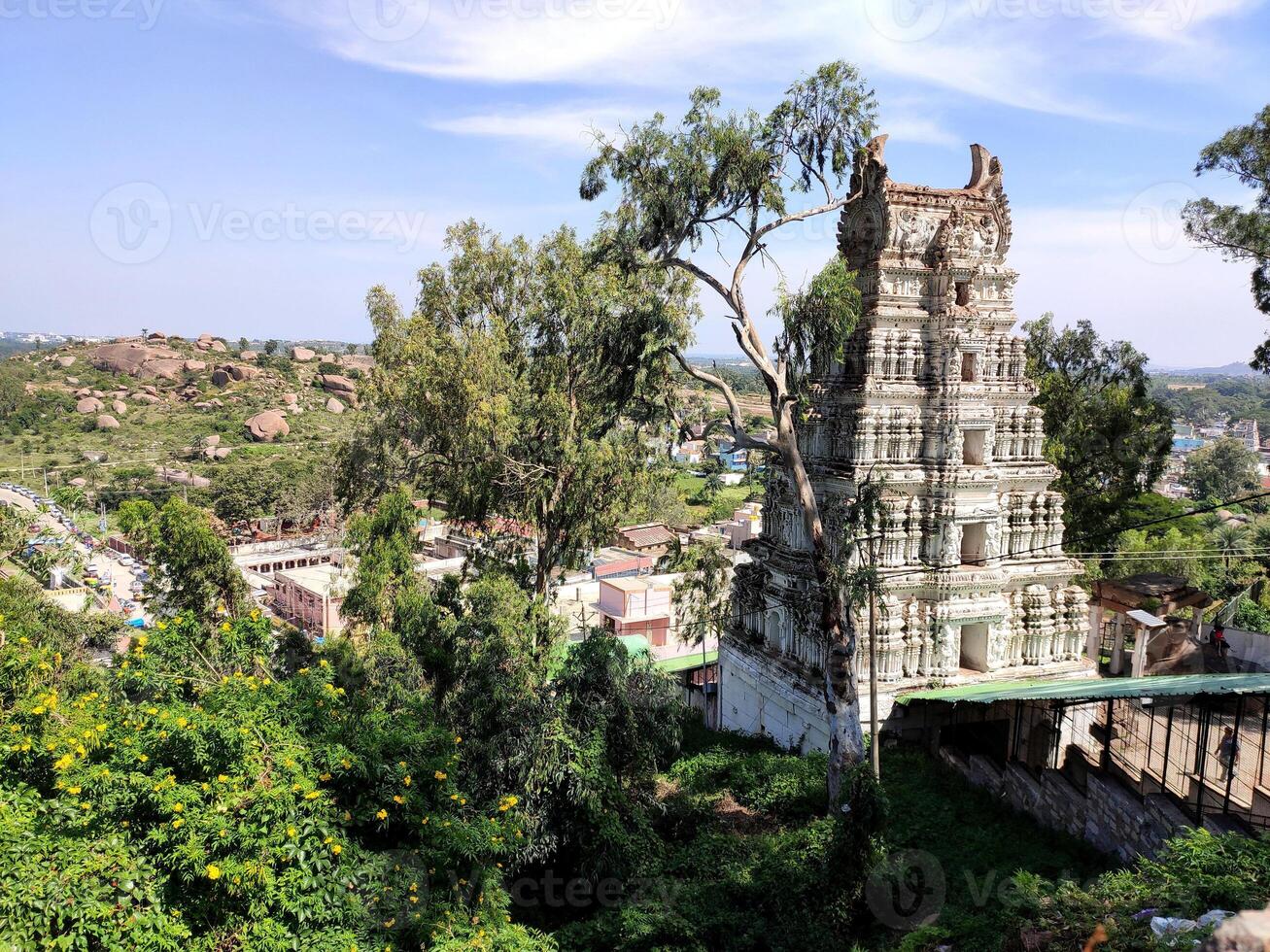 Shivagange hill temple, adorned with intricate carvings and a towering gopuram. The temple's white exterior stands out against the vibrant green hills and the bustling cityscape below. photo
