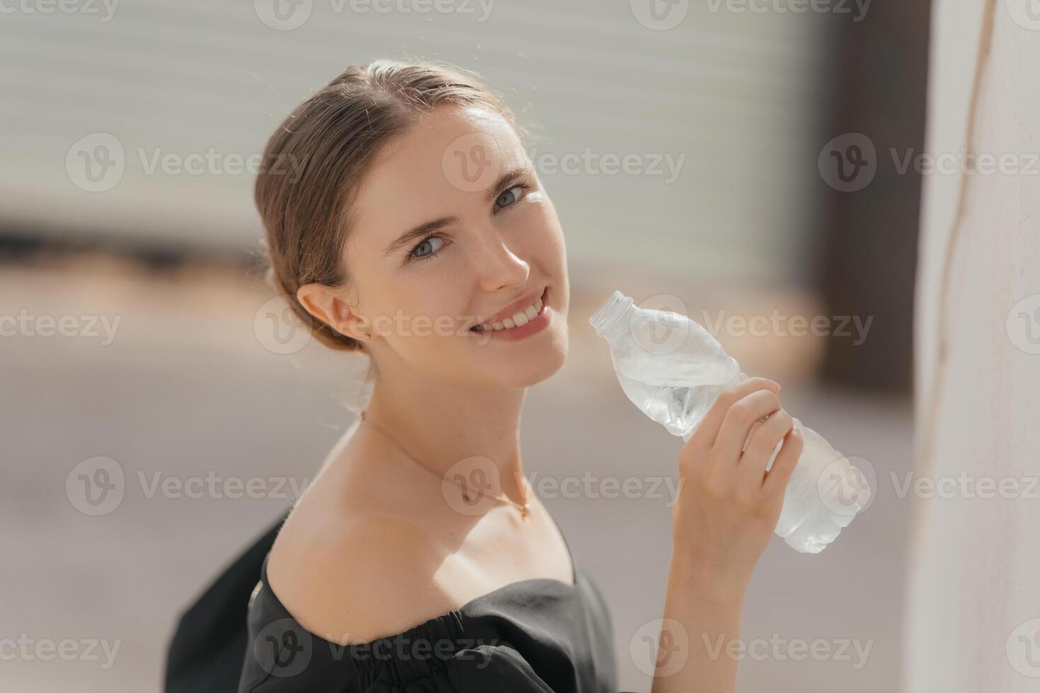 Close-up portrait of a beautiful young girl drinking water from the bottle. Street portrait. photo