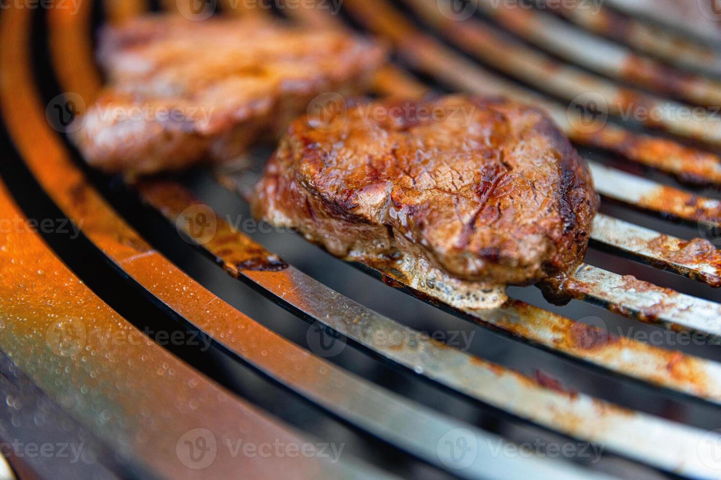 Juicy, seasoned meat steaks sizzle on a grill grate over burning coals, with flames and smoke rising as they cook to perfection. photo