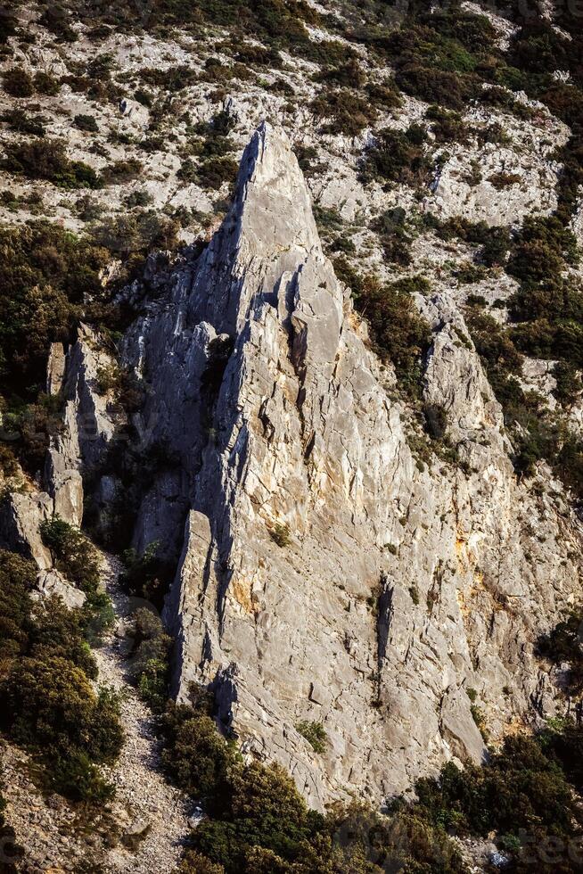 Teide National Park in Tenerife. A rugged volcanic landscape. A towering, jagged rock formation stands prominently in the center, surrounded by barren mountains and dry, rocky photo
