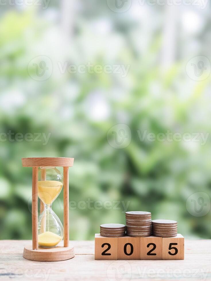 Hourglass, Wooden blocks with the number 2025 and stack of coins. The concept of saving money for manage time to success business in year 2025 photo