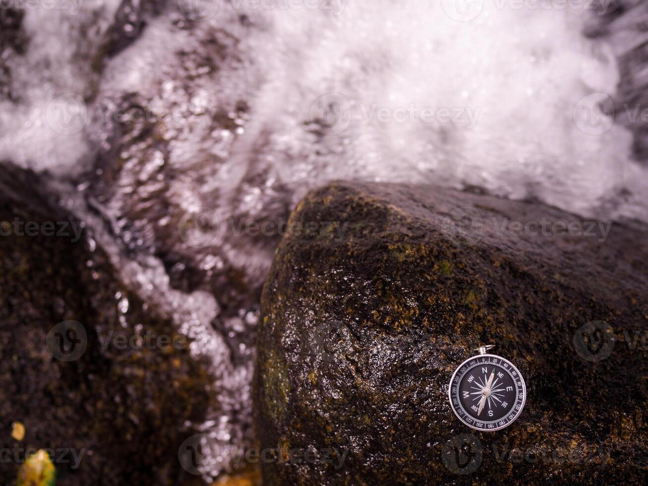 Compass on the rock with waterfall as background. The concept of world tourism day, Searching the right directions and Travel photo
