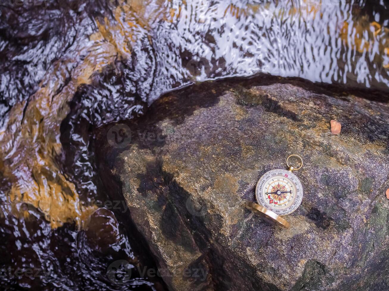 Compass on the rock with waterfall as background. The concept of world tourism day, Searching the right directions and Travel photo