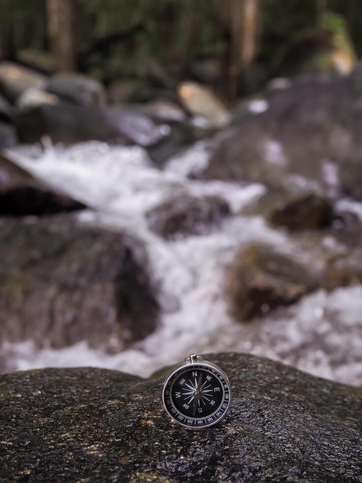 Compass on the rock with waterfall as background. The concept of world tourism day, Searching the right directions and Travel photo
