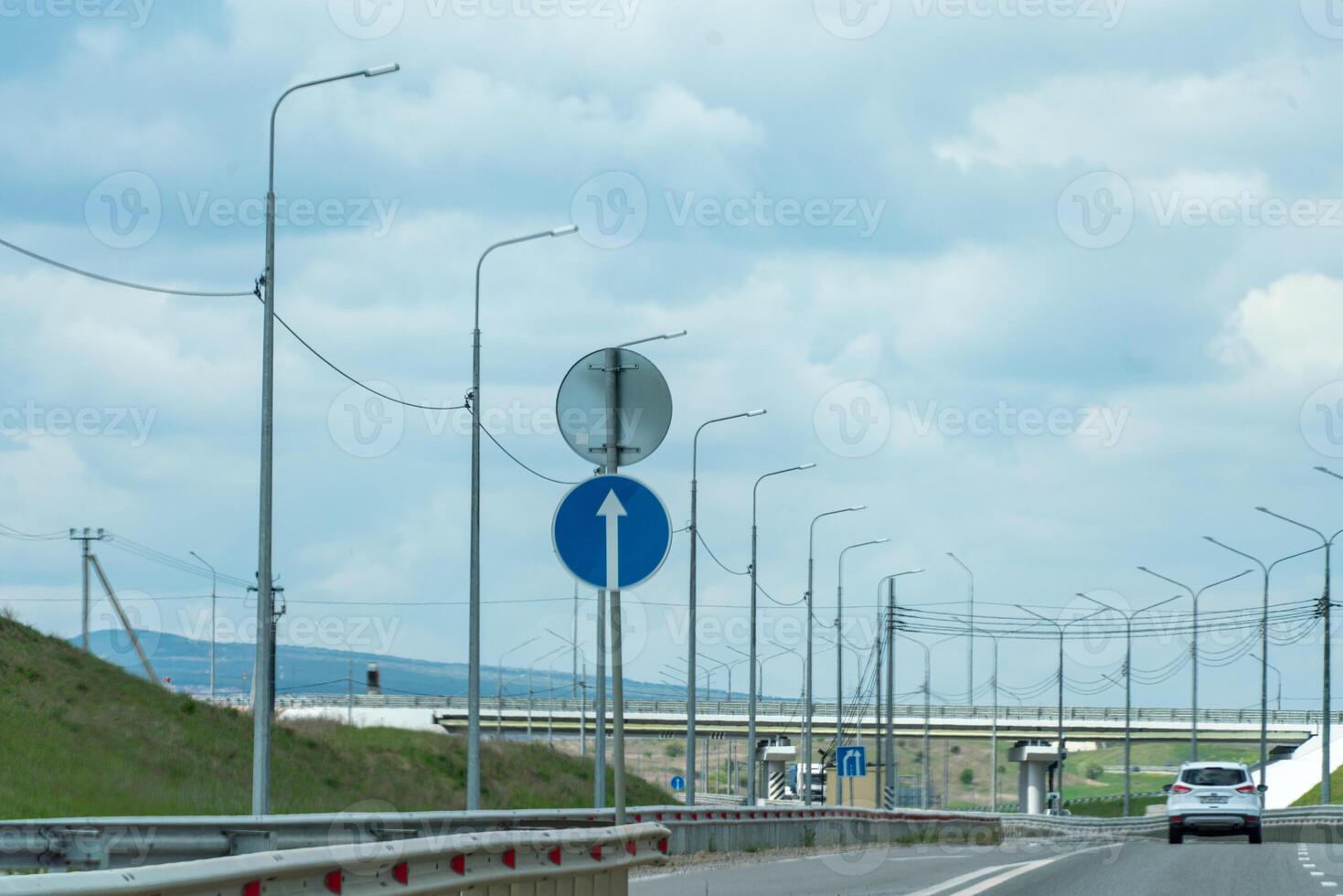 A road with a blue sign pointing to the right. The sky is cloudy and the road is empty. photo