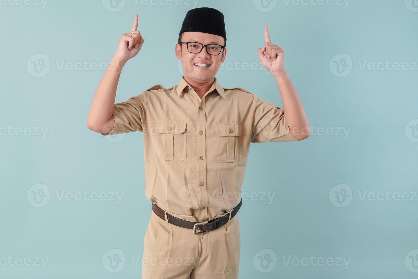 Smiling Indonesian government worker man wearing khaki uniform pointing to the copy space upwards. photo