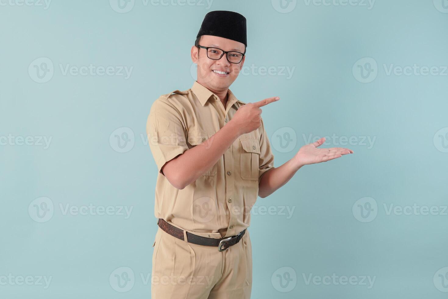 Happy Indonesian government worker man wearing khaki uniform pointing to the copy space beside him. photo