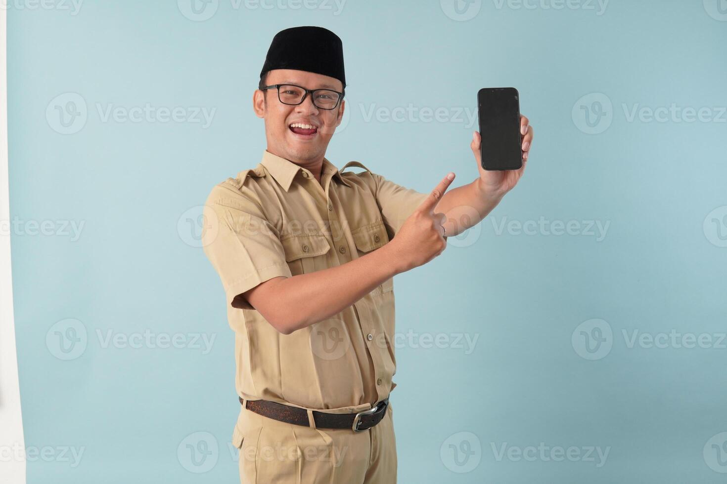 Excited Indonesian government worker man wearing khaki uniform presenting copy space on smartphone. photo