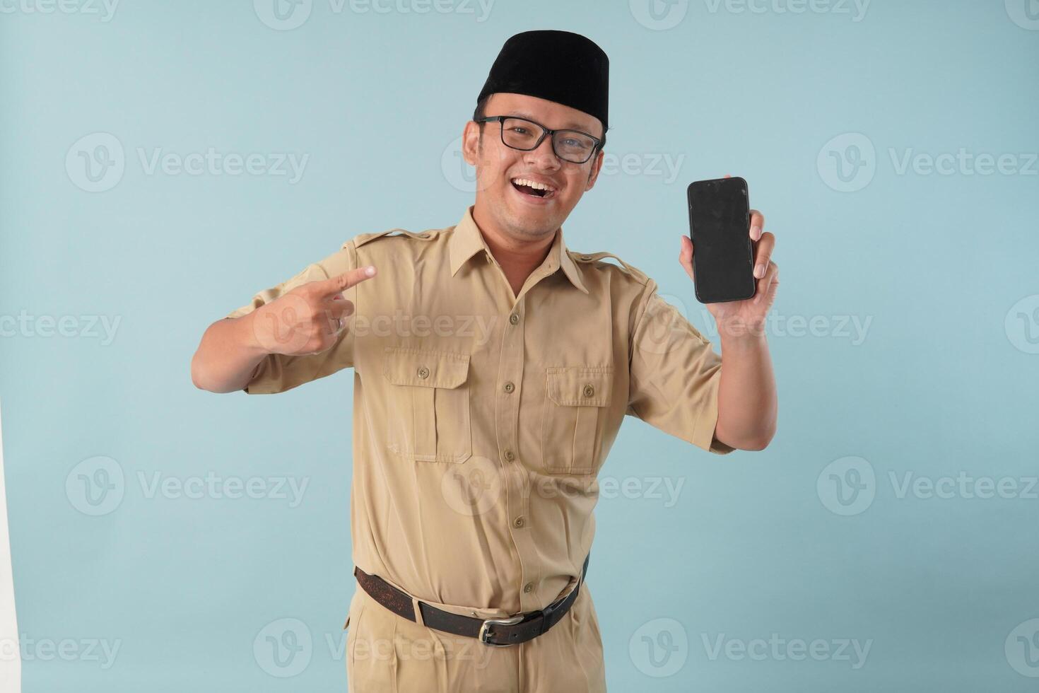Excited Indonesian government worker man wearing khaki uniform presenting copy space on smartphone. photo