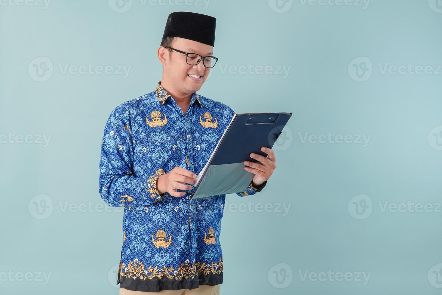 Handsome government worker man wearing blue batik uniform reading and checking document paper. photo