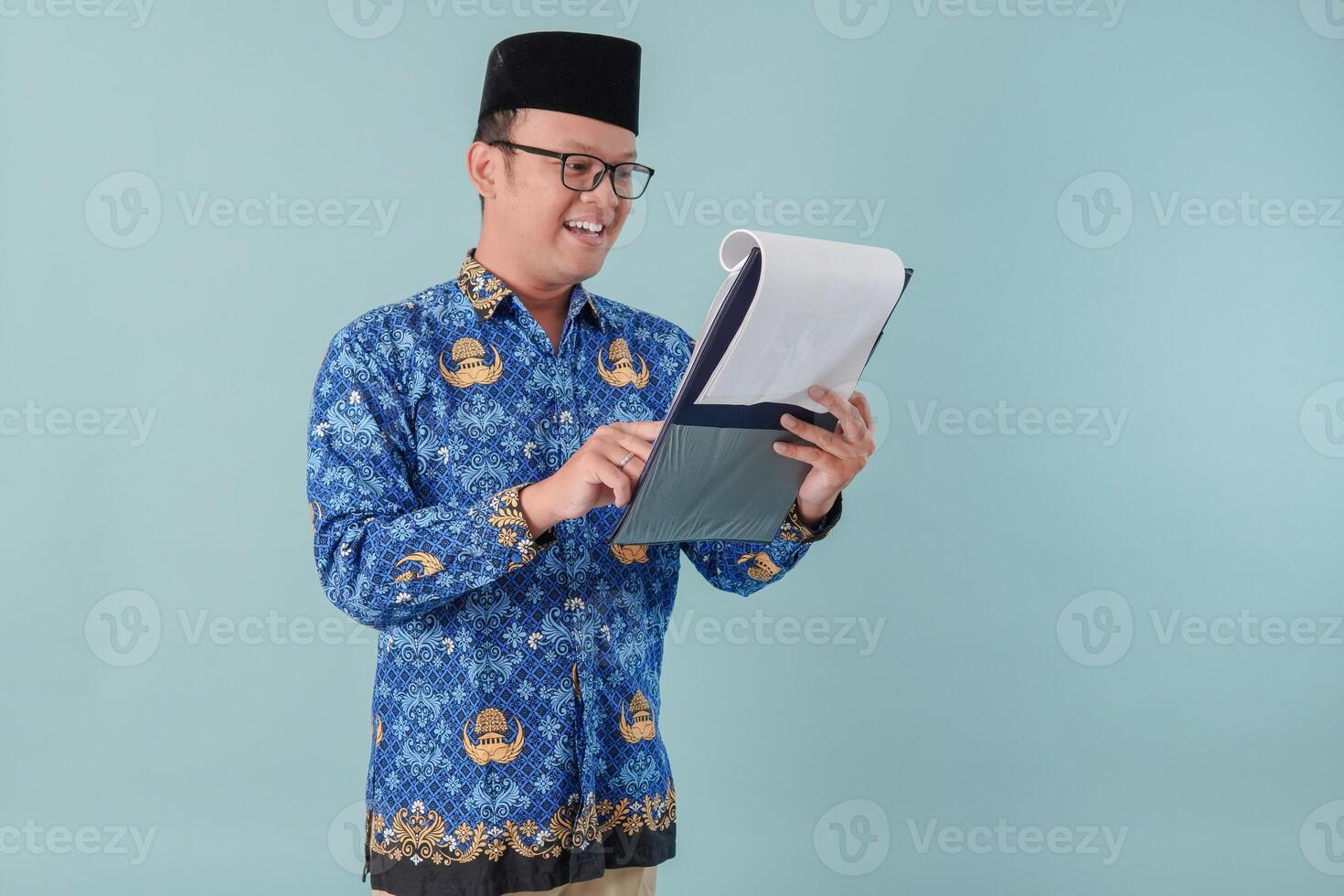 Handsome government worker man wearing blue batik uniform reading and checking document paper. photo